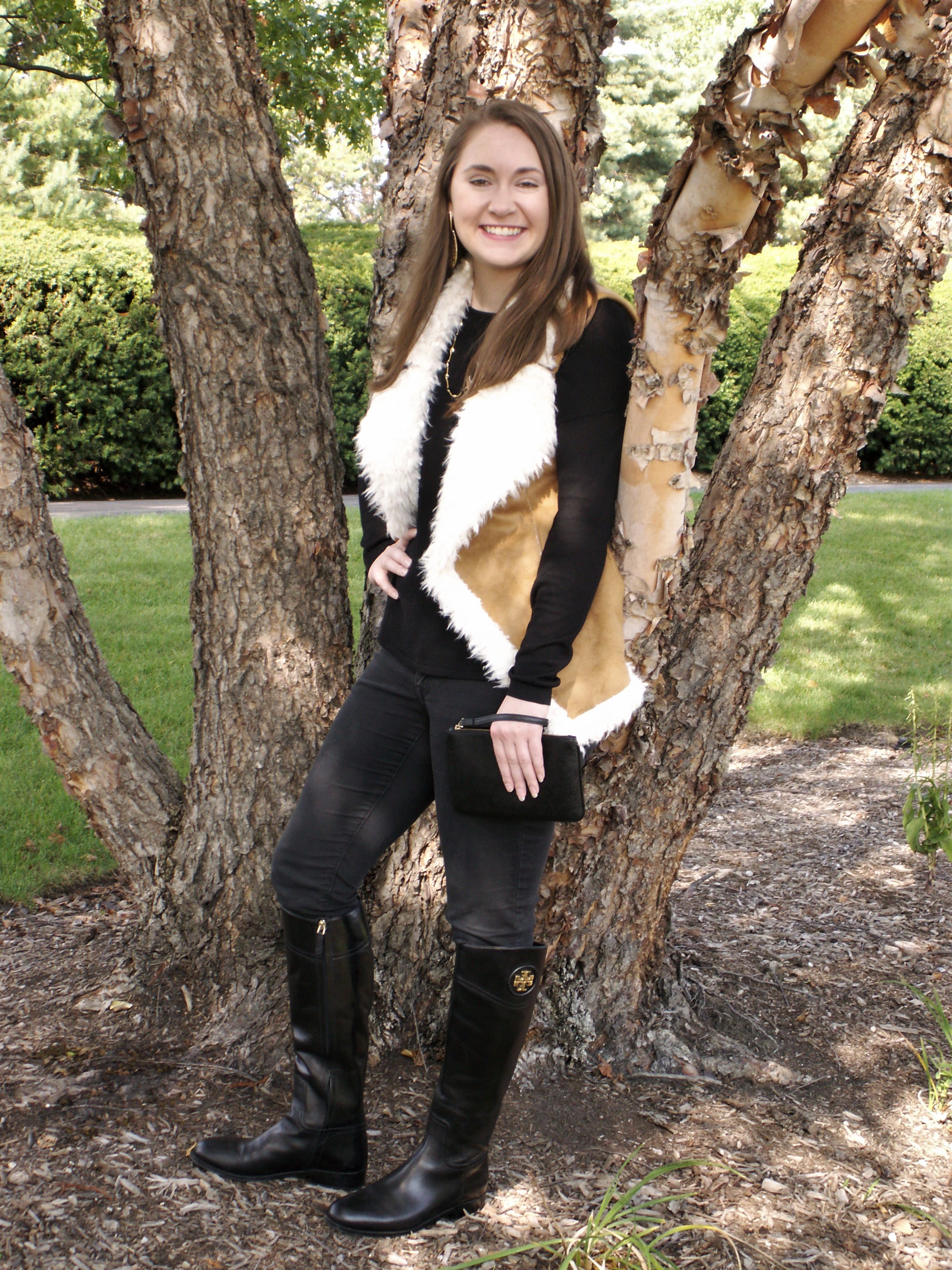 Model is wearing a shearling and suede vest over a black shirt and jeans with trendy accessories.